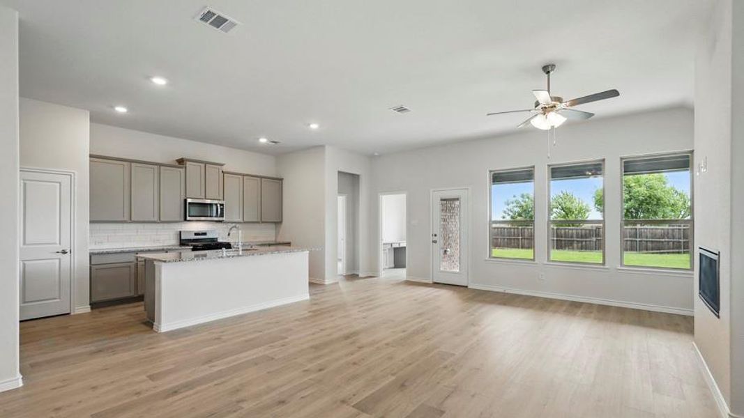 Kitchen with gray cabinets, open floor plan, a kitchen island with sink, light stone countertops, and stainless steel appliances
