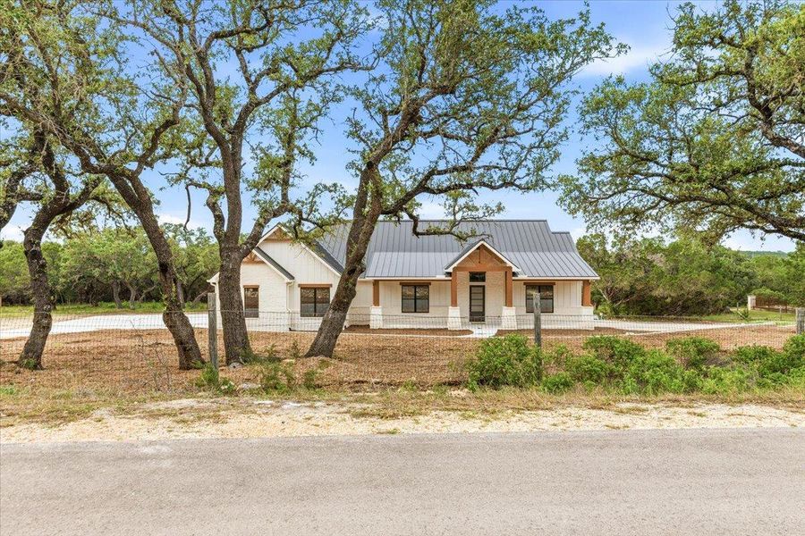 A newly constructed modern farmhouse with a durable metal roof is framed by mature trees, offering privacy and natural beauty.
