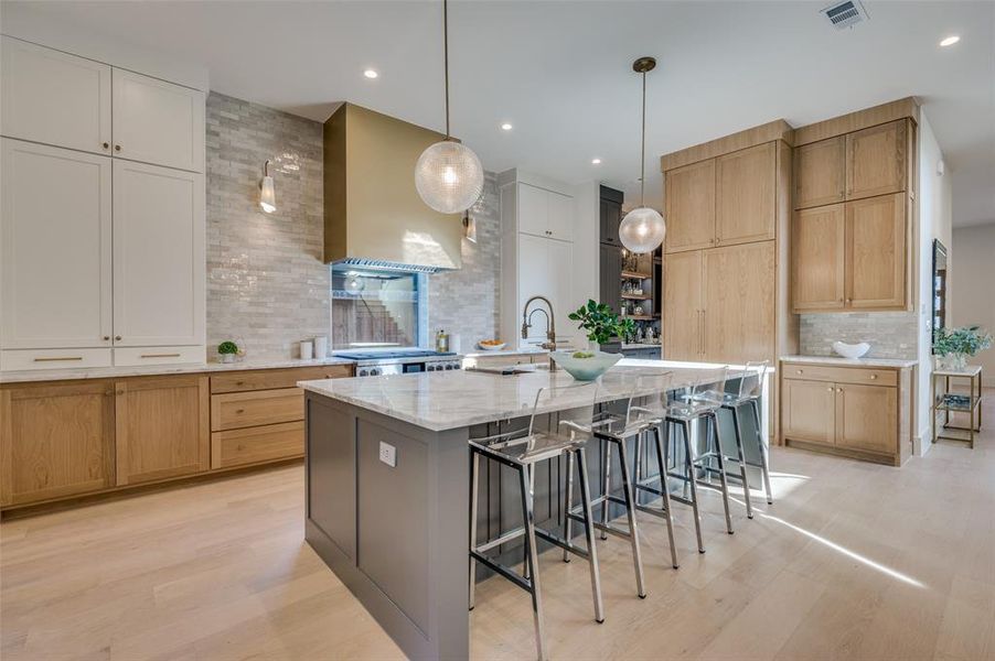 Kitchen with range hood, decorative backsplash, light stone countertops, hanging light fixtures, and a spacious island