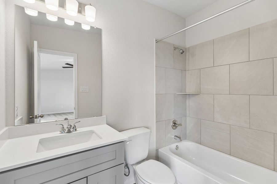 A modern vanity with stone counters complements a tiled tub and shower combination.