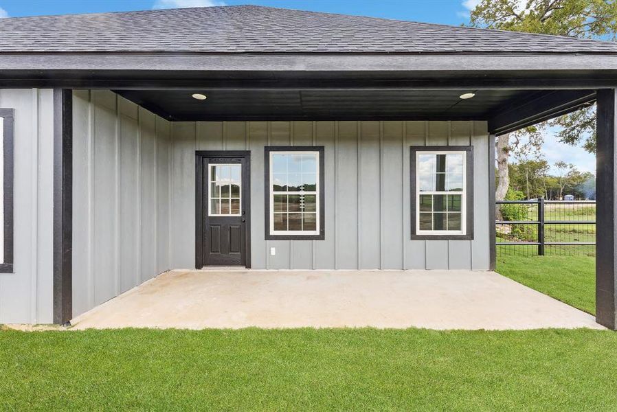Doorway to property featuring roof with shingles, a patio, and board and batten siding Doorway to property featuring roof with shingles, a patio, and board and batten siding