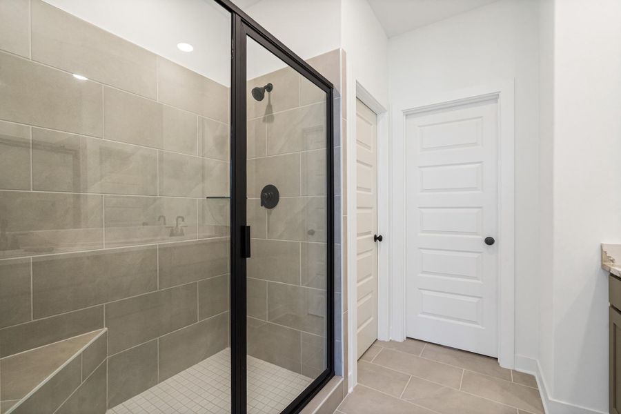 Walk-in shower with clear glass enclosure and matte black fixtures, featuring large format tile walls, a built-in bench, and a tiled floor Walk-in shower with clear glass enclosure and matte black fixtures, featuring large format tile walls, a built-in bench, and a tiled floor