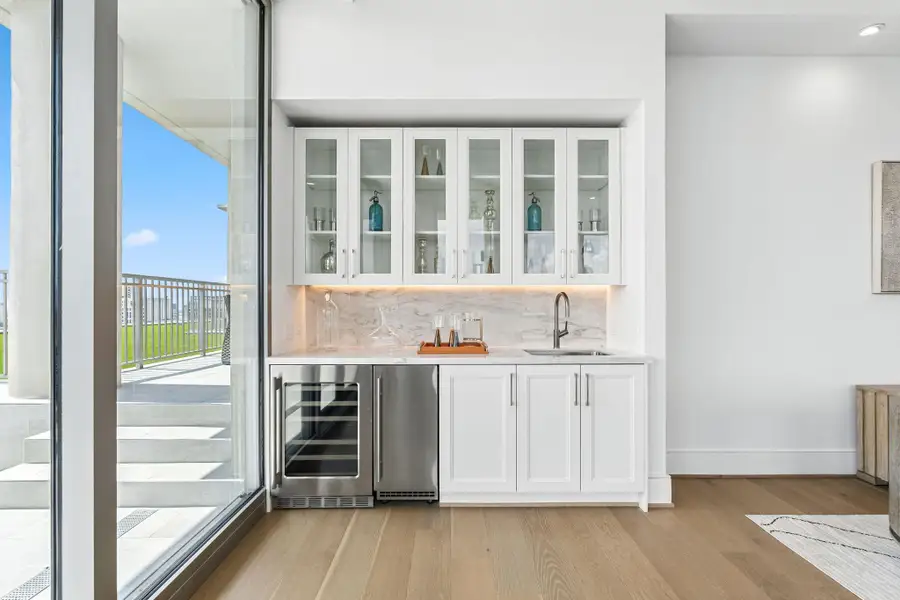 For your entertainment and as a part of the living space, enjoy this custom-built wet bar with under-cabinet lighting, glass enclosed cabinets, wine chiller, ice maker and a sink For your entertainment and as a part of the living space, enjoy this custom-built wet bar with under-cabinet lighting, glass enclosed cabinets, wine chiller, ice maker and a sink