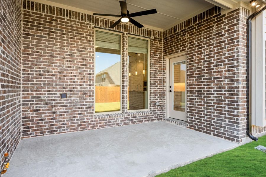 Covered back patio with brick walls, ceiling fan, concrete floor, and glass door entry Covered back patio with brick walls, ceiling fan, concrete floor, and glass door entry