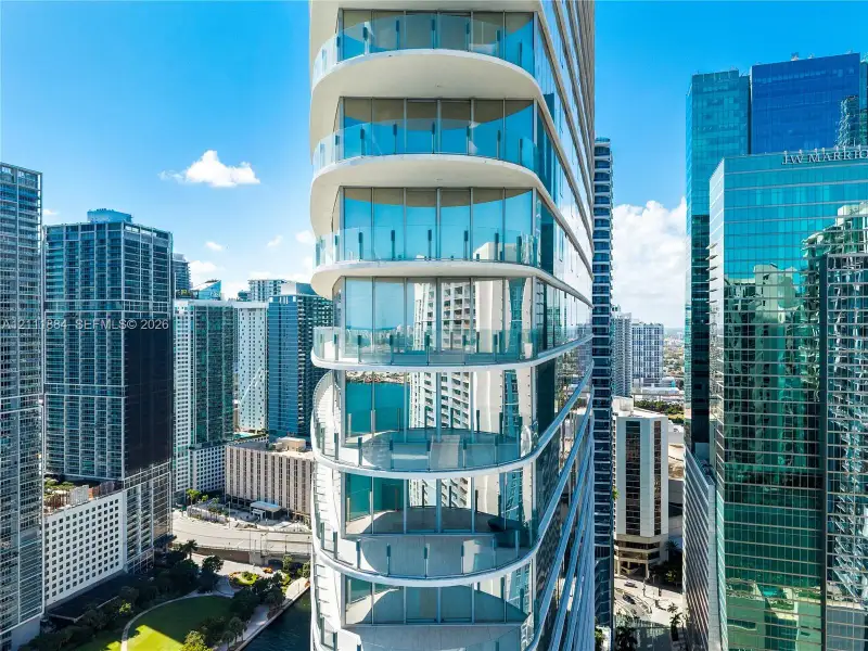 High-rise architectural exterior featuring tiered, curved structural design, floor-to-ceiling glass wall systems, and wrap-around glass panel balcony railings High-rise architectural exterior featuring tiered, curved structural design, floor-to-ceiling glass wall systems, and wrap-around glass panel balcony railings