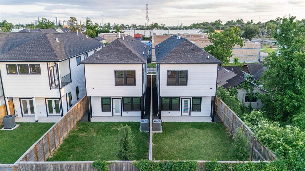 Modern, two-story home with white siding and dark accents. Spacious fenced backyard. View of the skyline in the background.