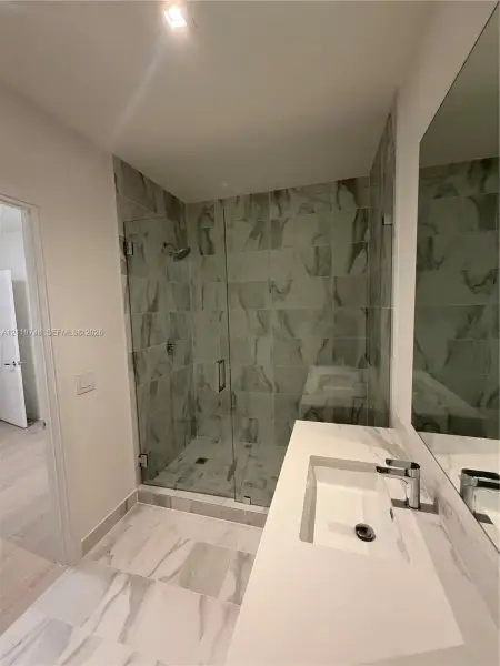 Walk-in shower with floor-to-ceiling tile, frameless glass enclosure, and wall-mounted shower head, paired with a white countertop vanity featuring an integrated rectangular sink and chrome hardware