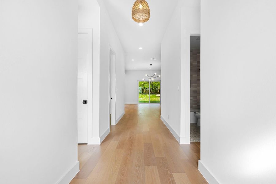 Corridor with light hardwood / wood-style floors and a notable chandelier Corridor with light hardwood / wood-style floors and a notable chandelier