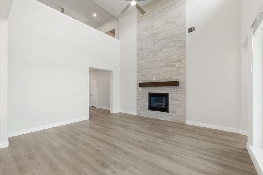 Open living room with high ceilings, tile-surround fireplace, wood mantel, and light hardwood floors Open living room with high ceilings, tile-surround fireplace, wood mantel, and light hardwood floors