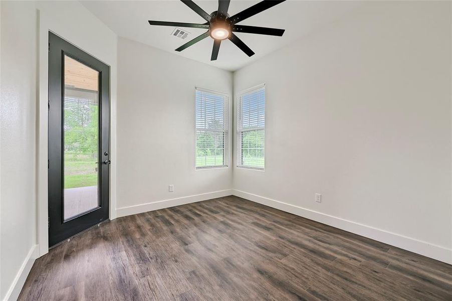 Spare room featuring dark wood-style flooring, ceiling fan, visible vents, and baseboards