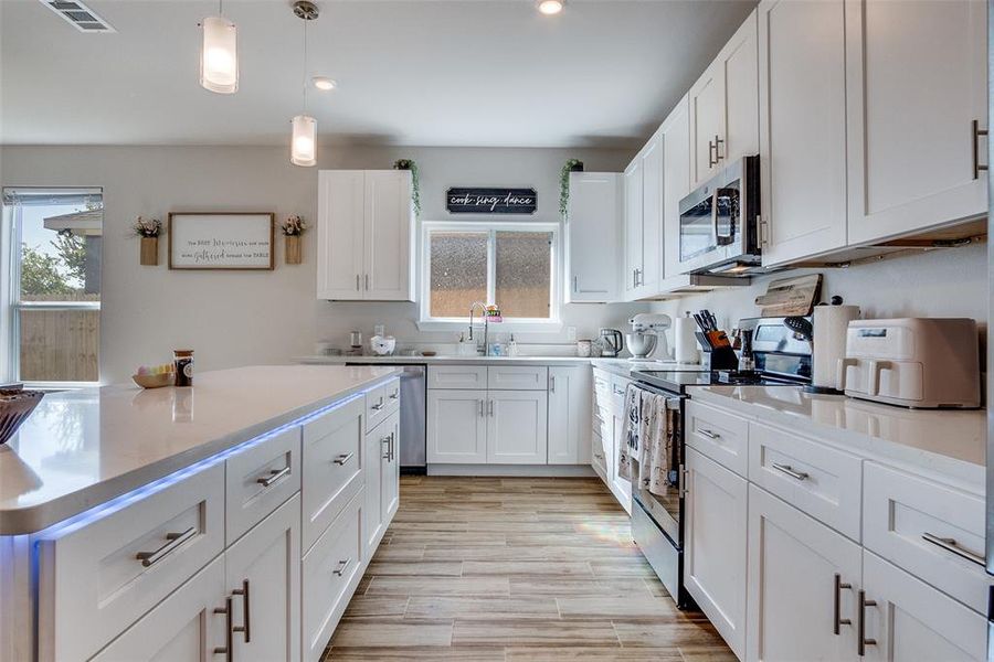 Kitchen featuring appliances with stainless steel finishes, hanging light fixtures, white cabinets, light wood finished floors, and light stone countertops