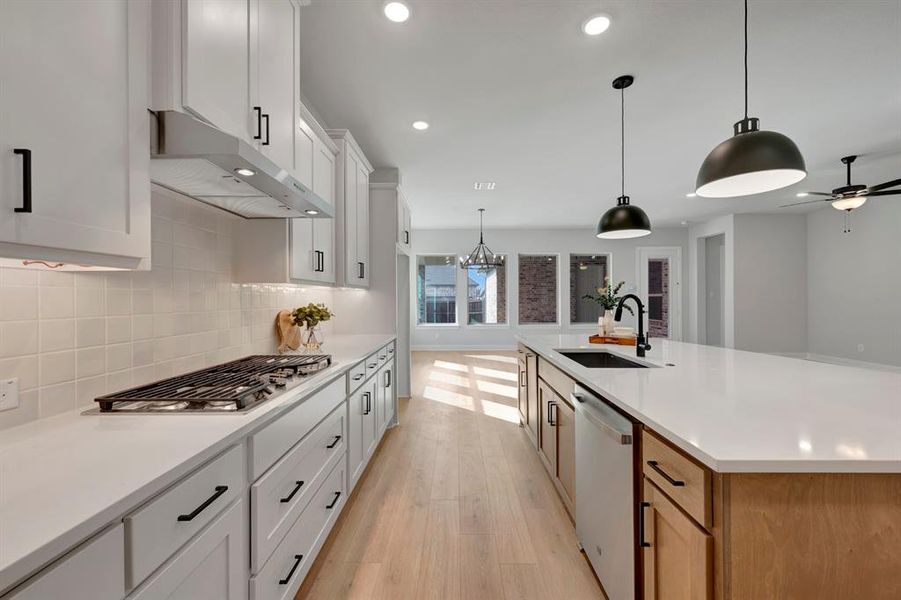 Kitchen featuring a spacious island, stainless steel appliances, light wood-type flooring, white cabinets, and decorative backsplash