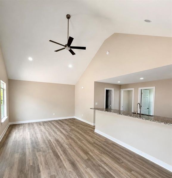 Spacious living area featuring a vaulted ceiling and wood-finish flooring Spacious living area featuring a vaulted ceiling and wood-finish flooring