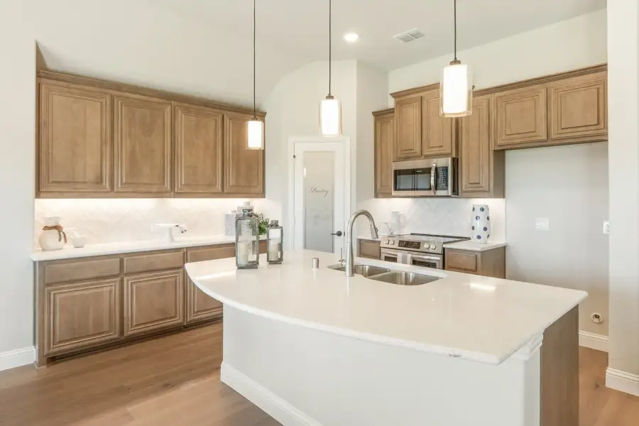 Kitchen with tan wood cabinets, white quartz island with sink, pendant lights, and stainless steel appliances