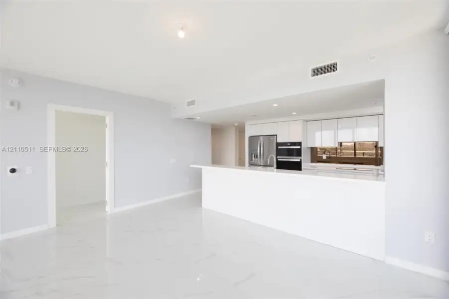 Open-concept area featuring white tile flooring with veining, white flat-panel cabinetry, a stone-surface peninsula, stainless steel appliances, and integrated recessed lighting