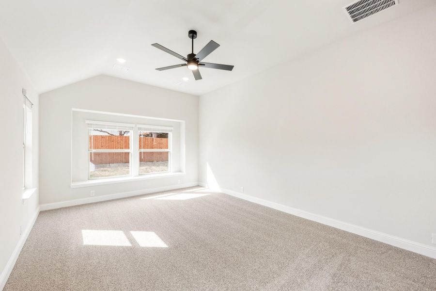Empty bedroom with vaulted ceiling, ceiling fan, carpet flooring, and large window Empty bedroom with vaulted ceiling, ceiling fan, carpet flooring, and large window