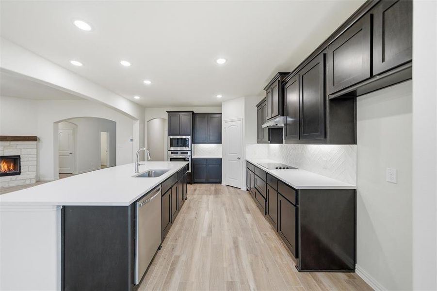 Kitchen featuring a stone fireplace, backsplash, recessed lighting, stainless steel appliances, and light wood-style floors