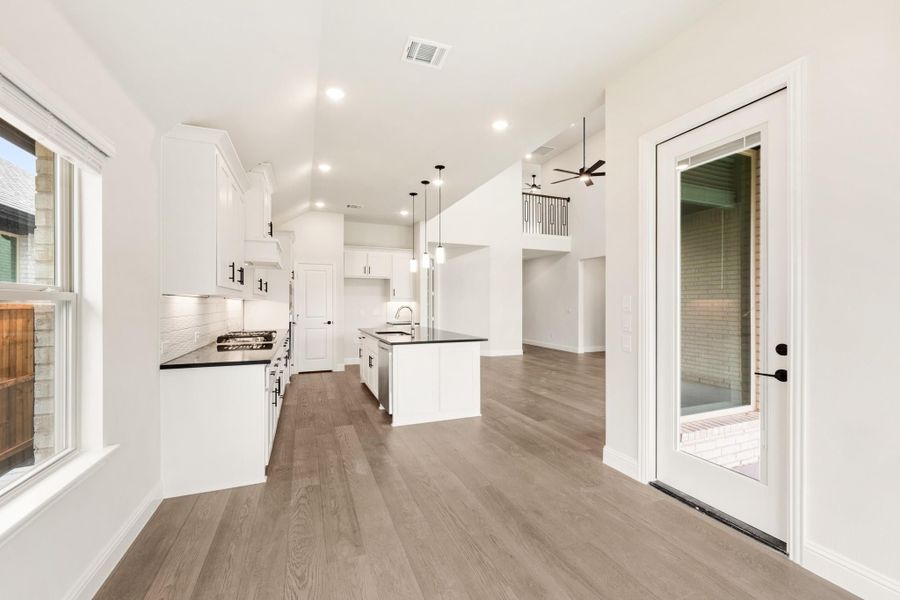 Open kitchen with white cabinets, dark countertops, center island, and hardwood floors leading to living area Open kitchen with white cabinets, dark countertops, center island, and hardwood floors leading to living area