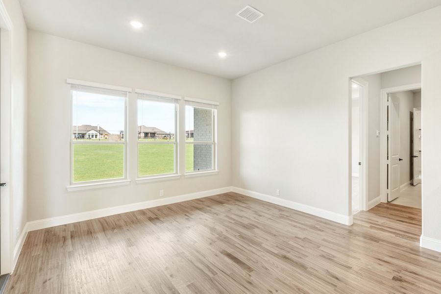 Empty bedroom with light wood floors, white walls, and three windows overlooking a grassy yard Empty bedroom with light wood floors, white walls, and three windows overlooking a grassy yard