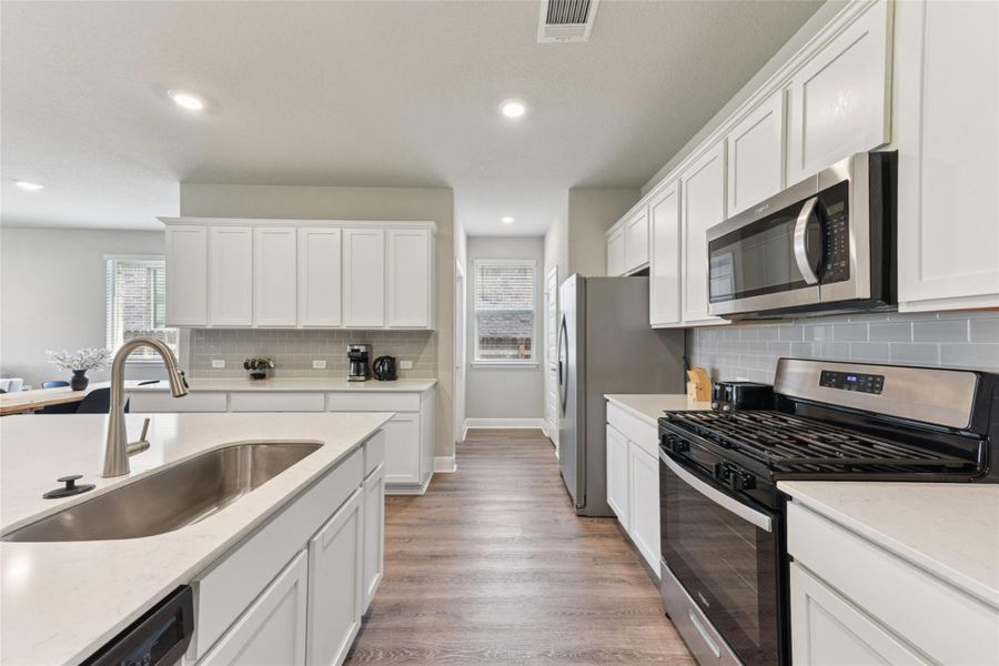 Kitchen with stainless steel appliances, light wood finished floors, tasteful backsplash, white cabinets, and recessed lighting Kitchen with stainless steel appliances, light wood finished floors, tasteful backsplash, white cabinets, and recessed lighting