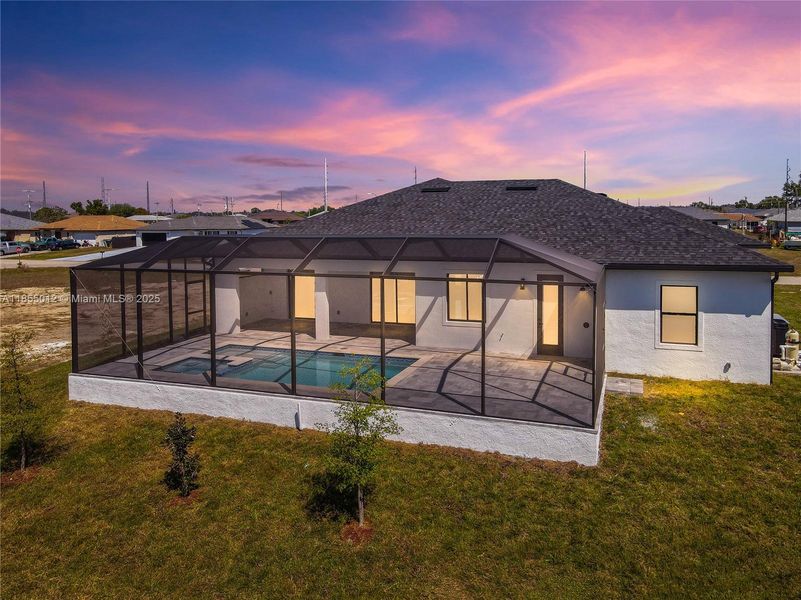 Back of house at dusk with Screened enclosure, stucco siding, a yard, and a patio area