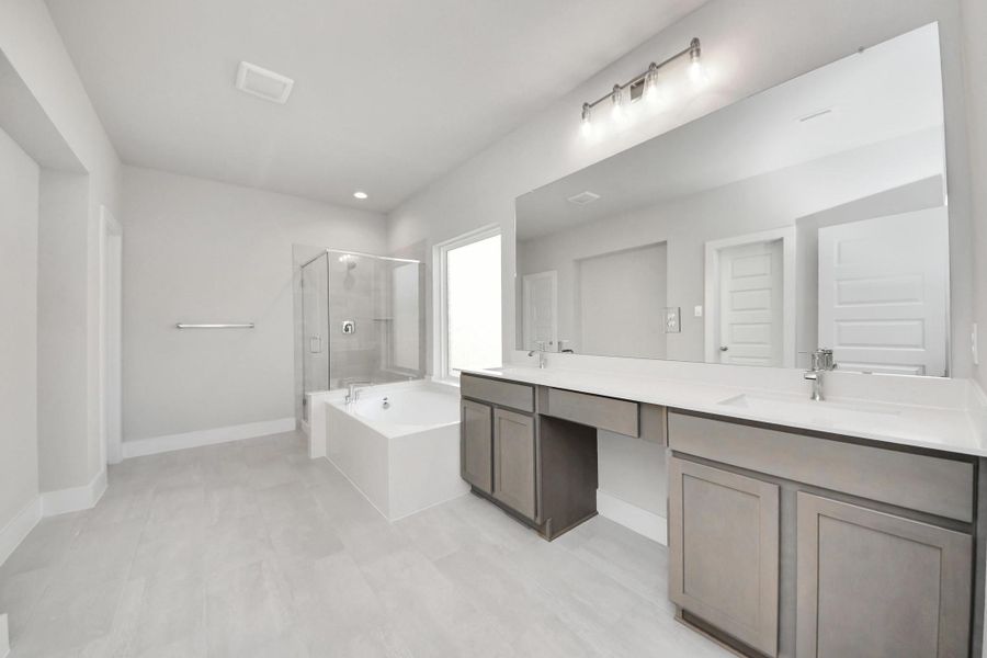Escape to a spa-like oasis in this primary bathroom. Enjoy a walk-in shower with tile surround, a separate garden tub with custom detailing, and an elegant vanity featuring light countertops, modern hardware, and beautiful vanity lights. Experience luxury and relaxation in every detail. Sample photo of completed home with similar floor plan. Actual colors and selections may vary.