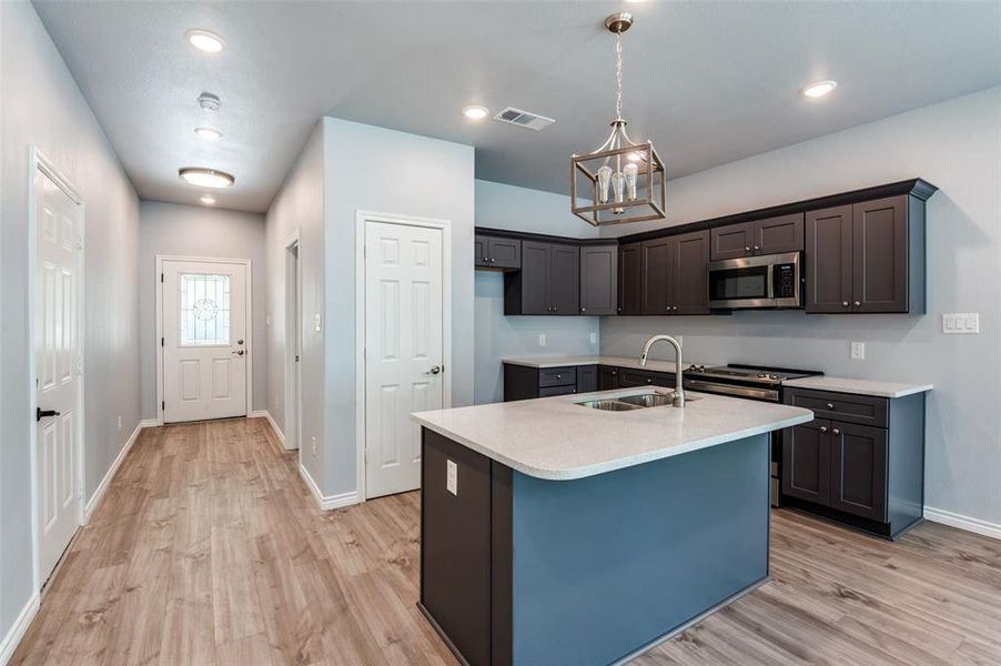 Kitchen with stainless steel appliances, pendant lighting, light wood-type flooring, sink, and a kitchen island with sink