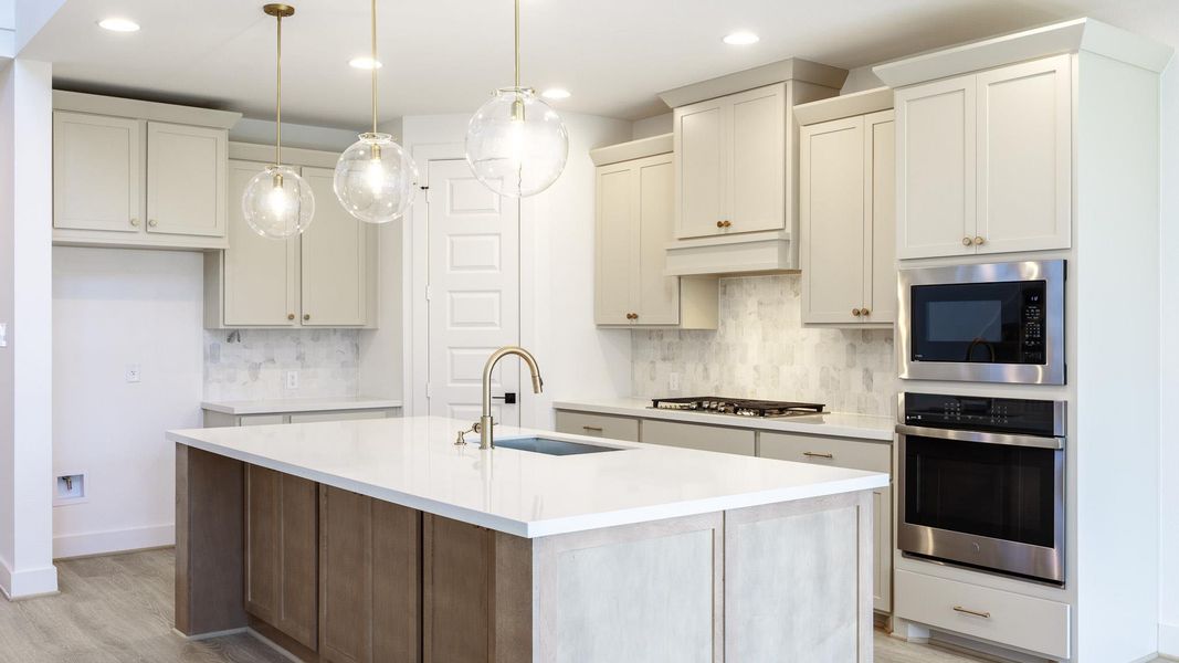 Kitchen with stainless steel appliances, light stone countertops, decorative backsplash, an island with sink, and decorative light fixtures Kitchen with stainless steel appliances, light stone countertops, decorative backsplash, an island with sink, and decorative light fixtures