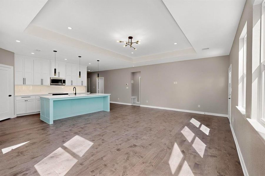 Kitchen featuring a tray ceiling, white cabinetry, decorative light fixtures, open floor plan, and a center island with sink Kitchen featuring a tray ceiling, white cabinetry, decorative light fixtures, open floor plan, and a center island with sink