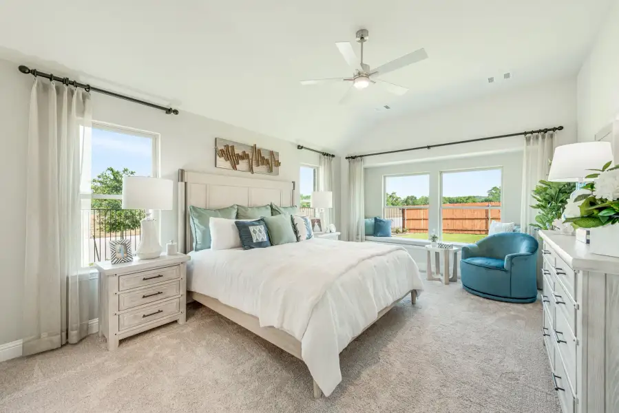 Spacious master bedroom with vaulted ceiling, ceiling fan, carpet flooring, and large windows with backyard views