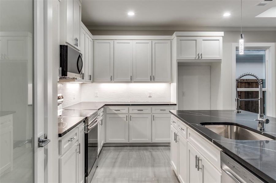 Kitchen featuring stainless steel appliances, hanging light fixtures, and white cabinets