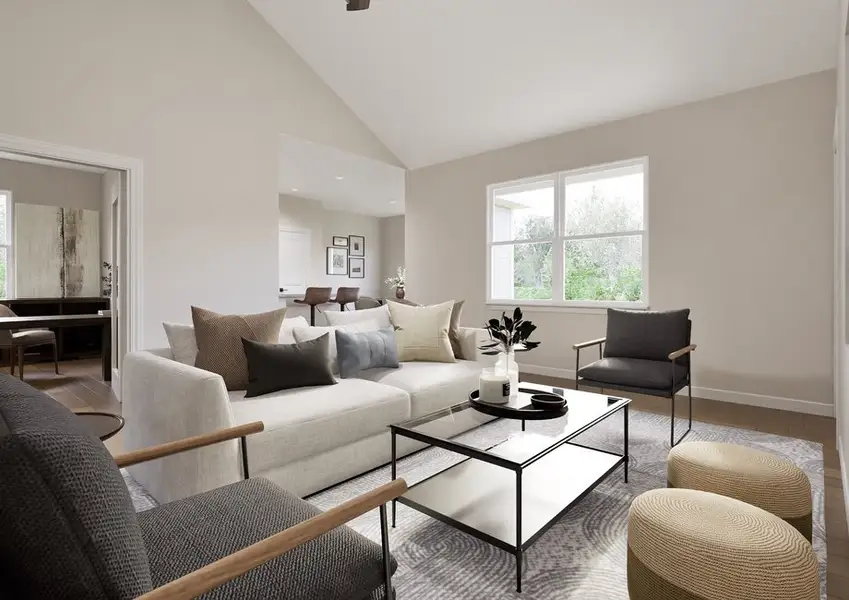 A modern living room with neutral tones featuring a white sofa, black chairs, and a glass coffee table. Sunlight streams through large windows, creating a serene ambiance.