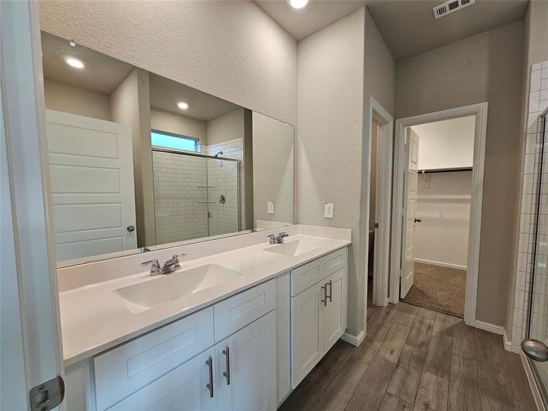 Full bathroom with a spacious closet, double sink, a stall shower, wood-looking tile flooring.