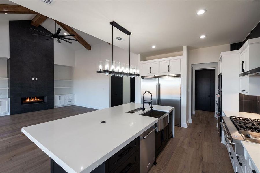 Kitchen featuring a tile fireplace, hanging light fixtures, lofted ceiling with beams, white cabinets, and a center island with sink