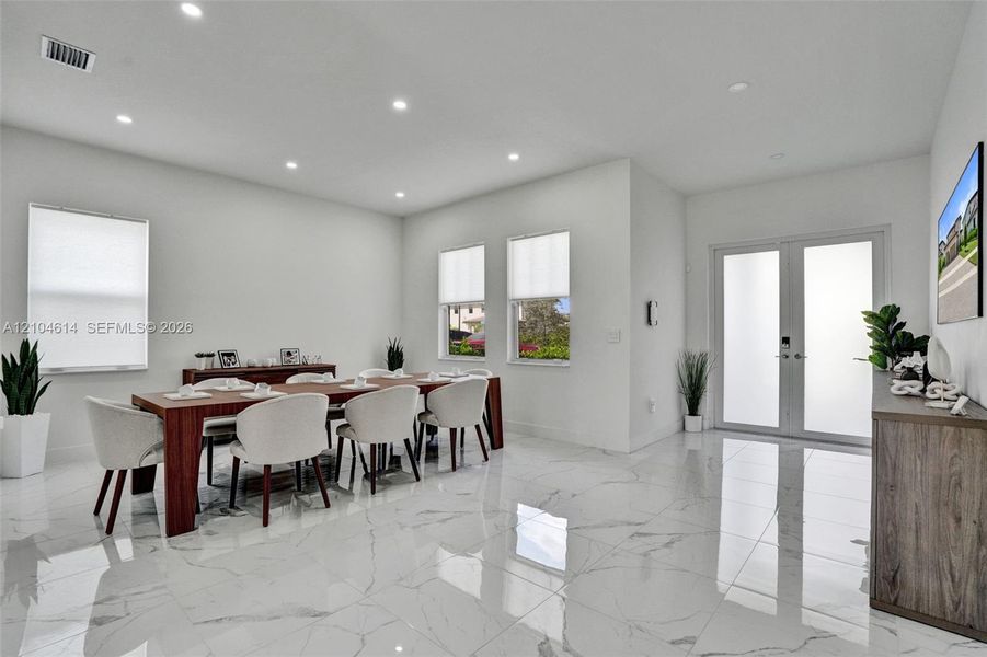Spacious room featuring large format marble-look tile flooring, recessed lighting, double frosted glass entry doors, and multiple windows
