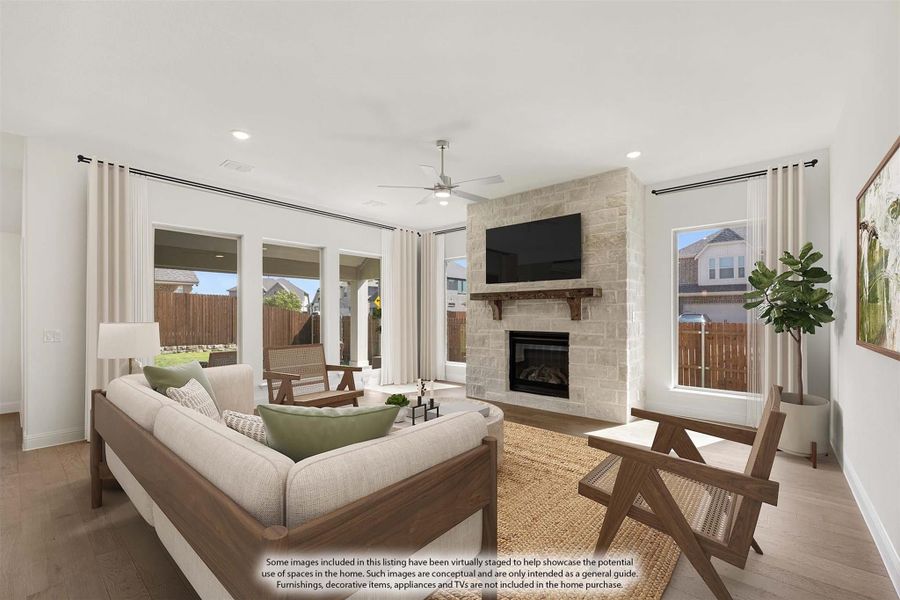 Living room with stone fireplace, wall-mounted TV, ceiling fan, and hardwood floors with large windows and patio access.