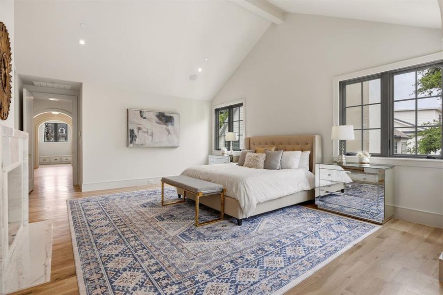 Bright bedroom featuring vaulted ceilings, light wood-finish flooring, and large windows with dark trim Bright bedroom featuring vaulted ceilings, light wood-finish flooring, and large windows with dark trim