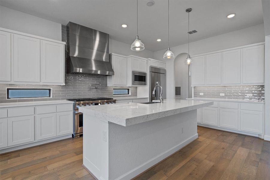 Gourmet kitchen featuring a large central island with a solid surface countertop, white shaker cabinetry, stainless steel appliances, a tiled backsplash, and wood-finish flooring