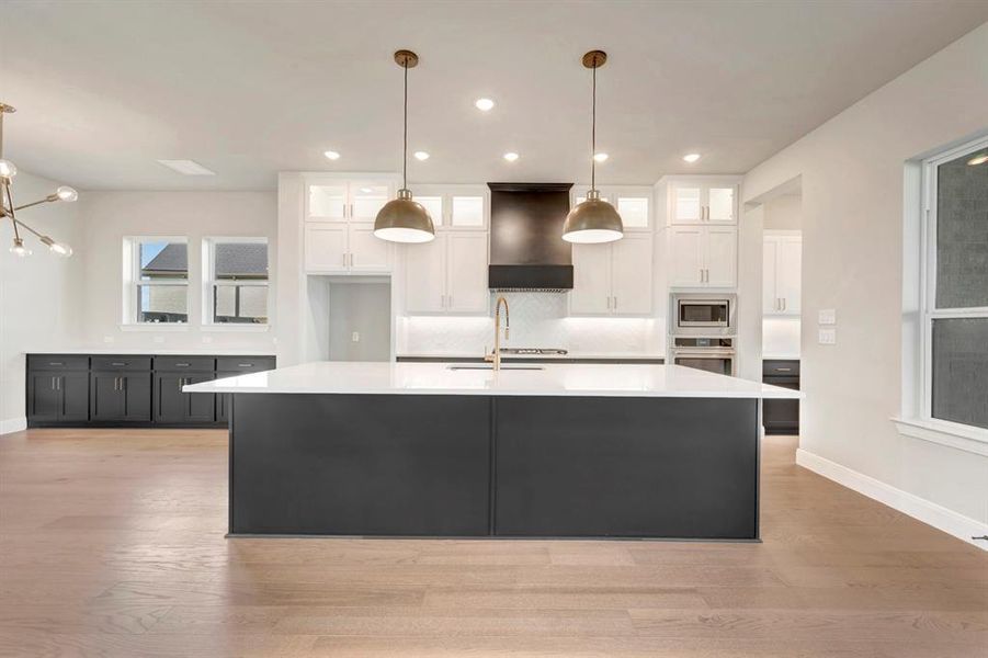Kitchen with dual tone cabinetry, glass insert cabinets, light wood finished floors, a large island with sink, and pendant lighting Kitchen with dual tone cabinetry, glass insert cabinets, light wood finished floors, a large island with sink, and pendant lighting