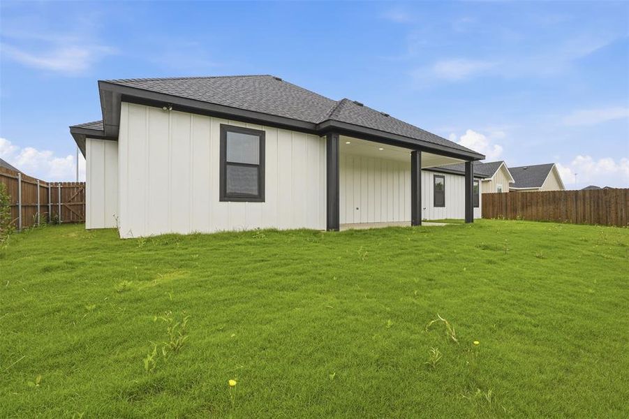 Spacious backyard with a covered patio, board and batten siding, dark-framed windows, and a privacy fence