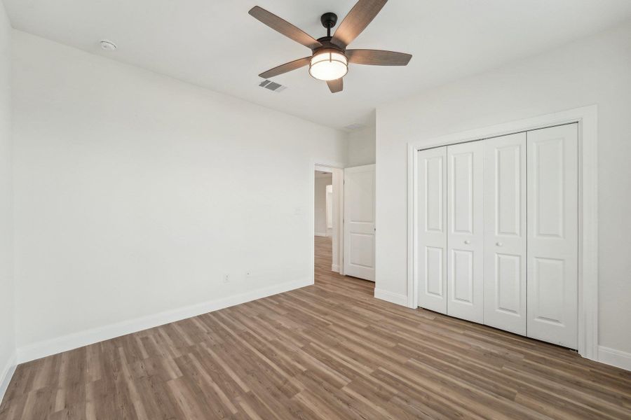 Bedroom 2 with wood plank vinyl floor, visible vents, a ceiling fan, a closet, and baseboards Bedroom 2 with wood plank vinyl floor, visible vents, a ceiling fan, a closet, and baseboards