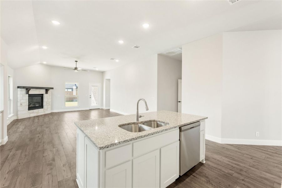 Kitchen island with granite countertop and sink, open to living room with fireplace and hardwood floors