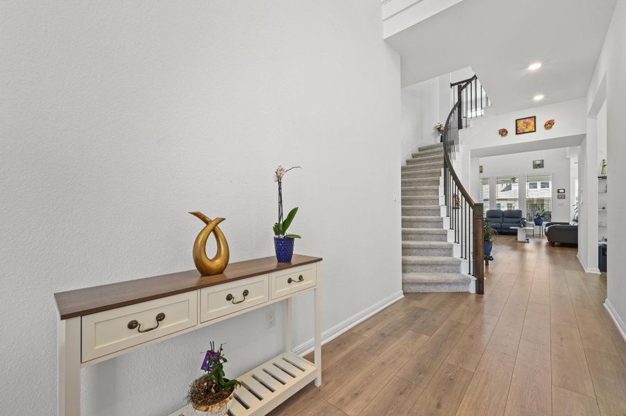 A soaring ceiling rises above the wood flooring leading past a curved staircase.