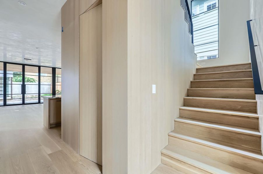 Blonde wood stairs lead to upper levels, complemented by sleek light wood paneling.