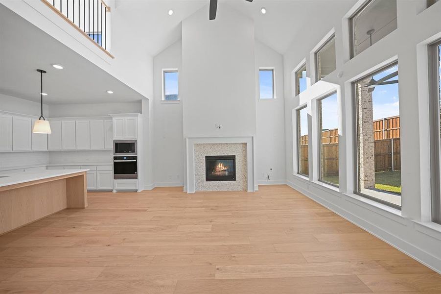 Unfurnished living room featuring high vaulted ceiling, recessed lighting, light wood finished floors, a glass covered fireplace, and ceiling fan
