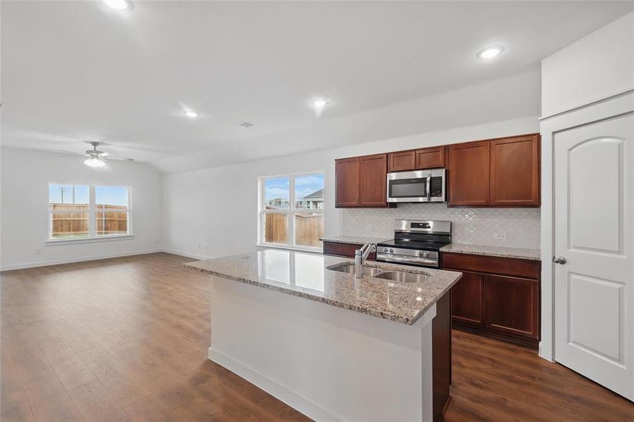 Kitchen with stainless steel appliances, light stone counters, a kitchen island with sink, dark wood-type flooring, and decorative backsplash Kitchen with stainless steel appliances, light stone counters, a kitchen island with sink, dark wood-type flooring, and decorative backsplash