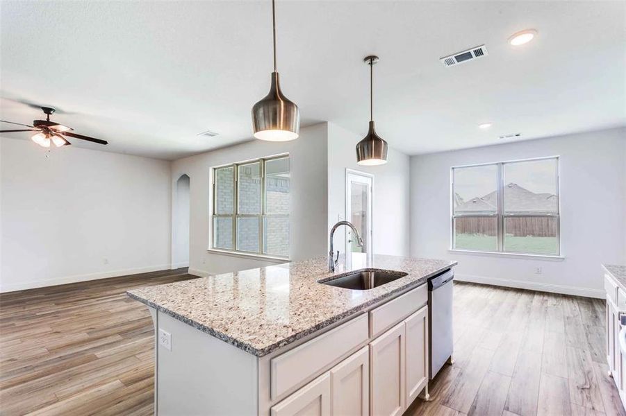 Kitchen with light stone counters, white cabinets, decorative light fixtures, dishwasher, and light hardwood / wood-style floors