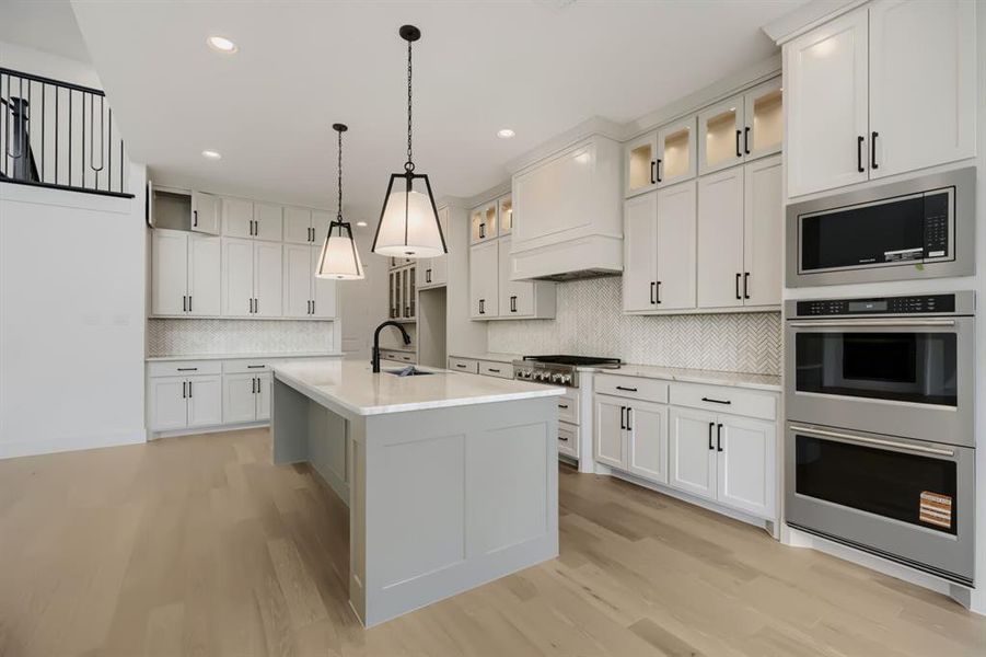 Open-concept kitchen featuring an oversized island with a quartz countertop, white shaker cabinetry, stainless steel appliances, and wood-finish flooring Open-concept kitchen featuring an oversized island with a quartz countertop, white shaker cabinetry, stainless steel appliances, and wood-finish flooring
