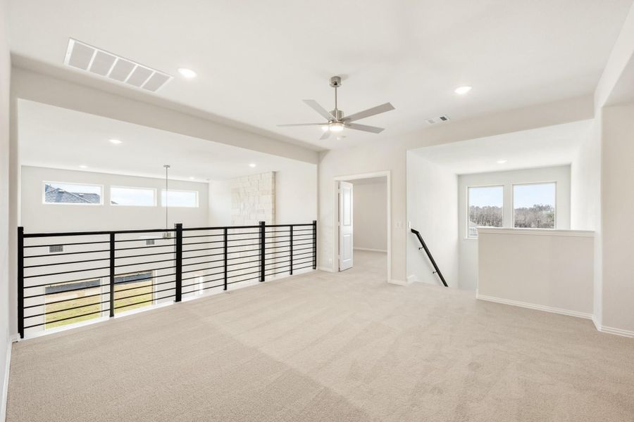Open upstairs loft with carpet, ceiling fan, and black metal railing overlooking lower level Open upstairs loft with carpet, ceiling fan, and black metal railing overlooking lower level