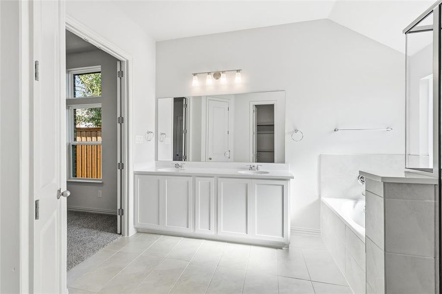 Full bathroom featuring double vanity, a garden tub, lofted ceiling, and light tile patterned floors